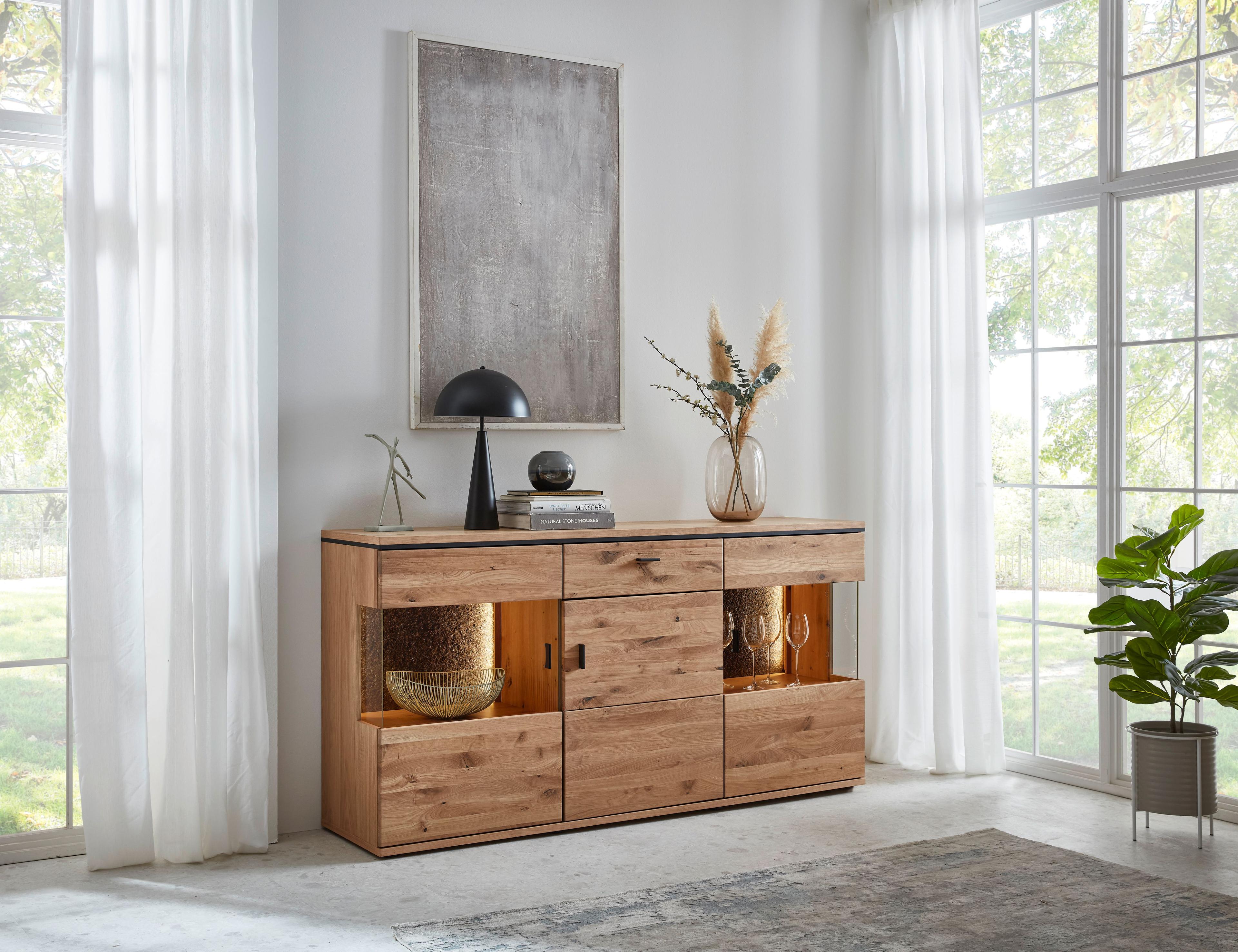 Sideboard mit 3 Türen, linke und rechte Tür jeweils mit mittigem Glasausschnitt, sichtbare Rückwände mit Steinfurnier und Beleuchtung